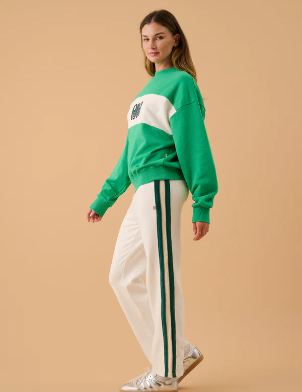 Woman wearing a green and white sweater with white pants against a beige background