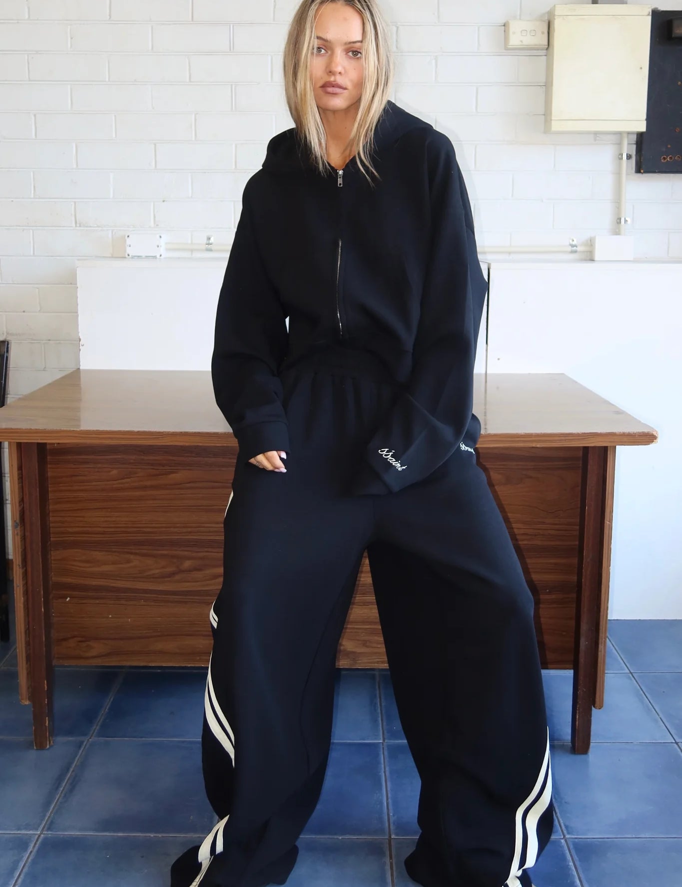 Woman wearing a black cropped zip hoodie and oversized striped track pants