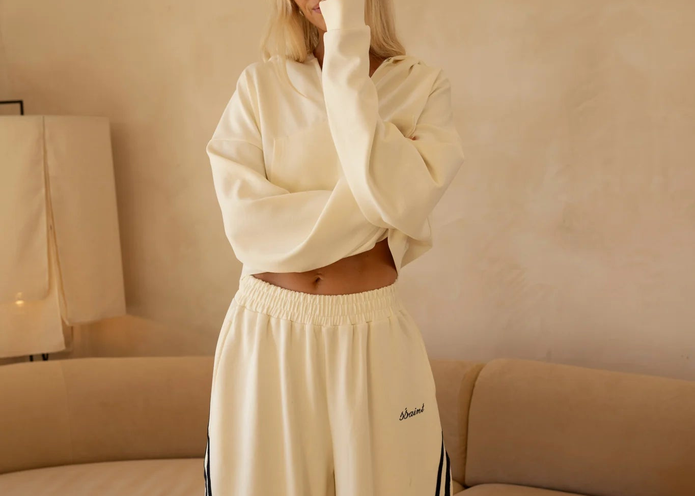 Woman wearing butter cream SSAINT wide-leg track pants with contrast side stripes