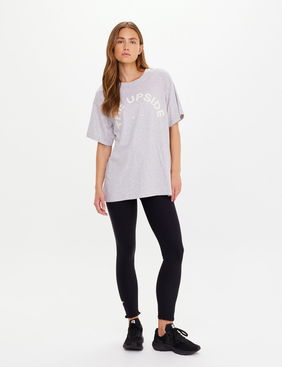 Woman wearing a light gray oversized t-shirt with text and black leggings on a white background