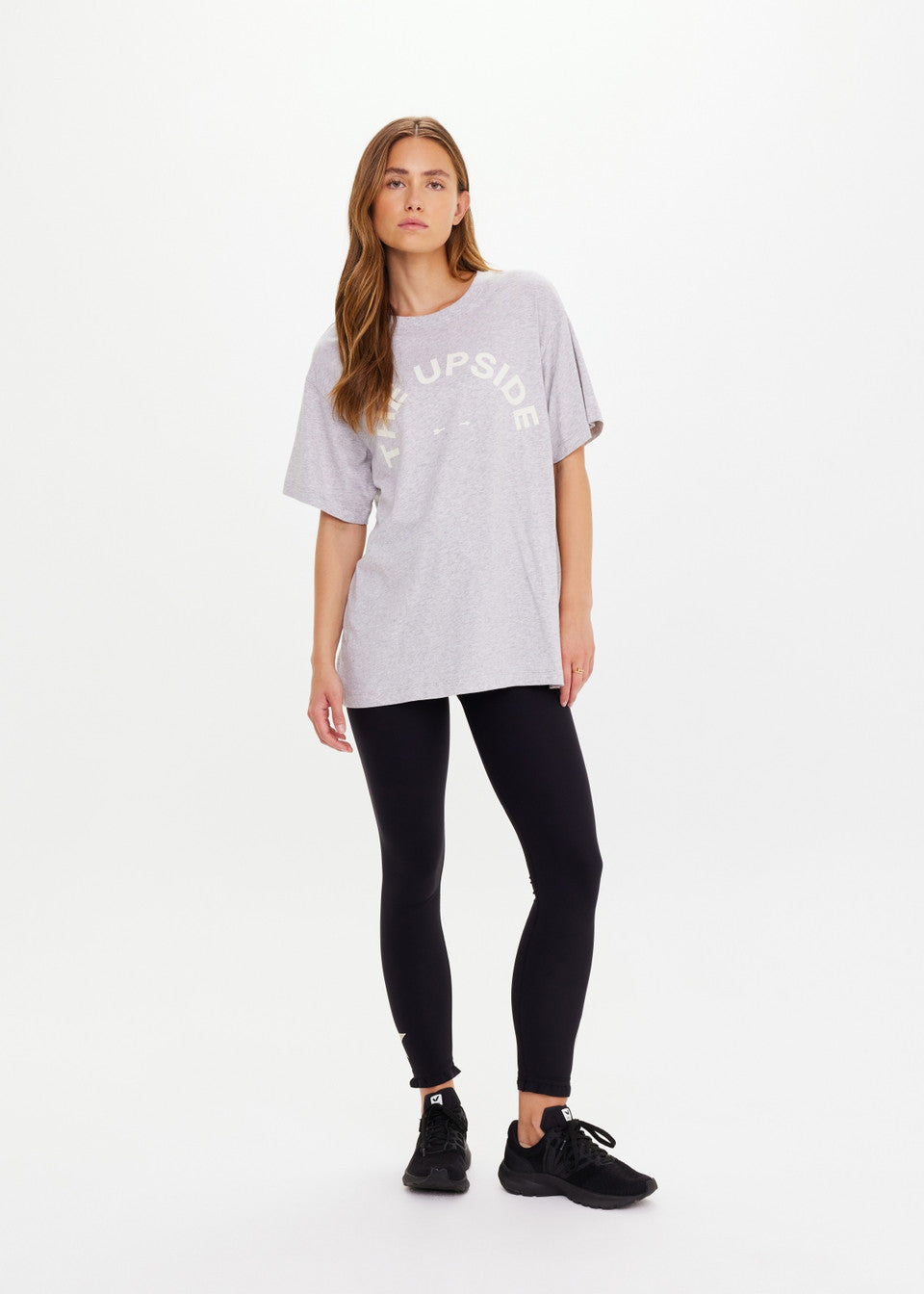 Woman wearing a light gray oversized t-shirt with text and black leggings on a white background
