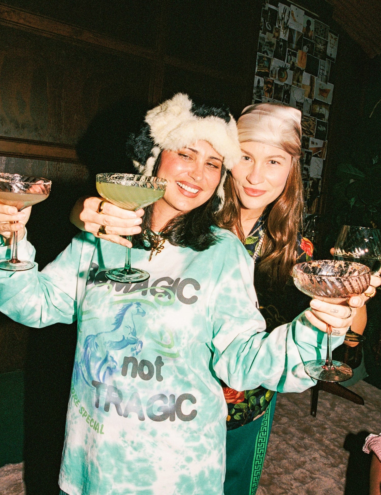 Two women in festive hats holding drinks in a cozy indoor setting