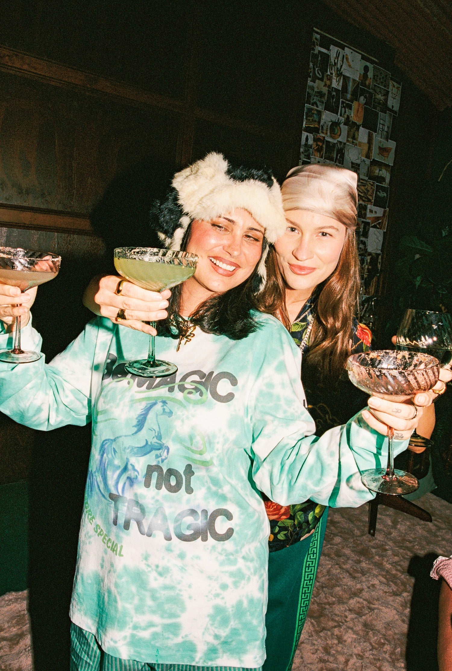 Two women in festive hats holding drinks in a cozy indoor setting
