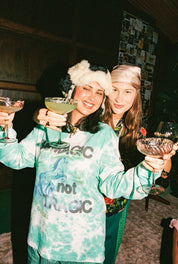 Two women in festive hats holding drinks in a cozy indoor setting
