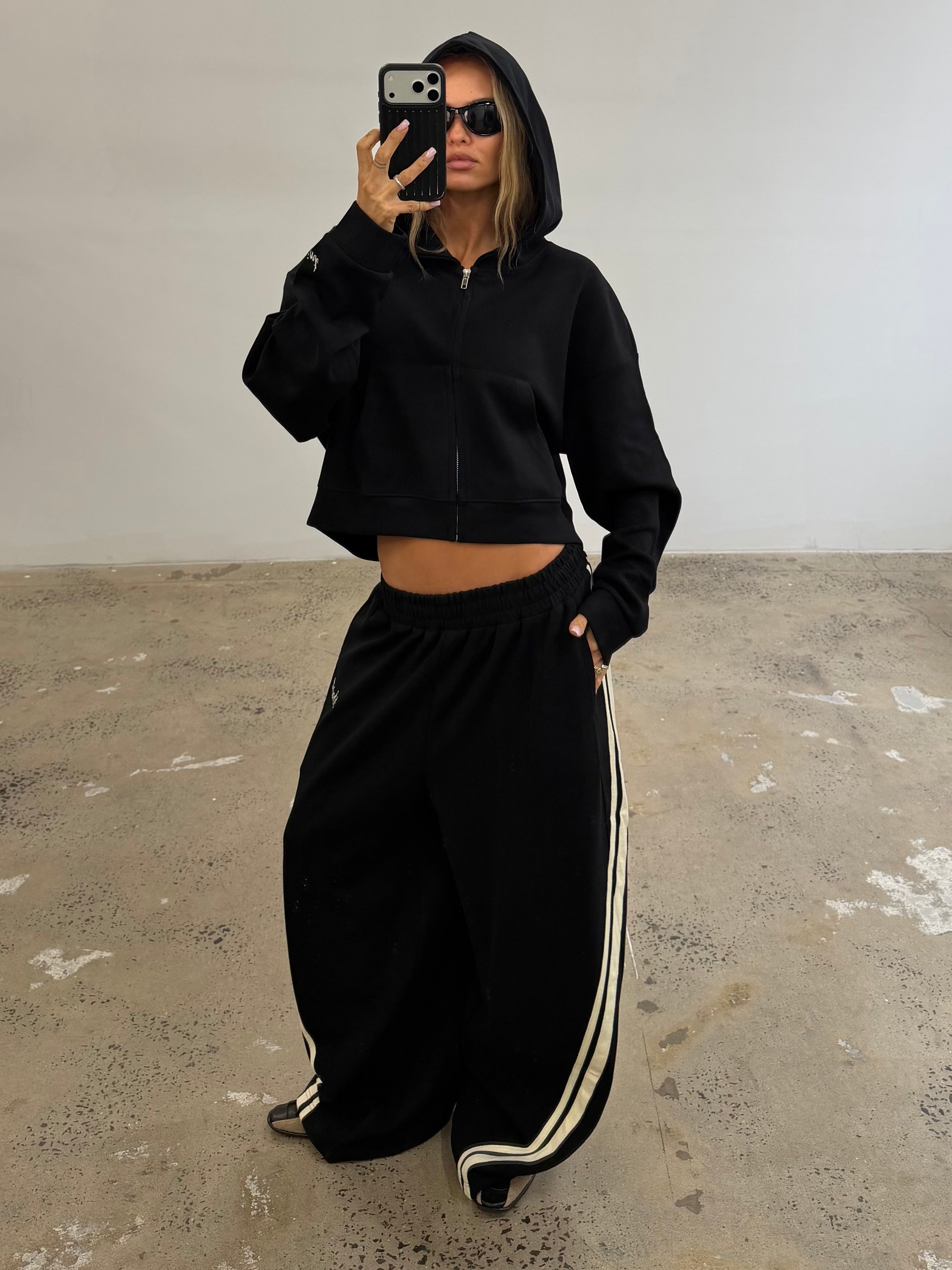 Woman wearing a black cropped hoodie and wide-leg track pants with side stripes