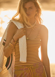Woman in a striped top and skirt holding a towel, standing against a bright background