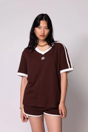 Woman wearing a brown outfit with white accents on a plain background