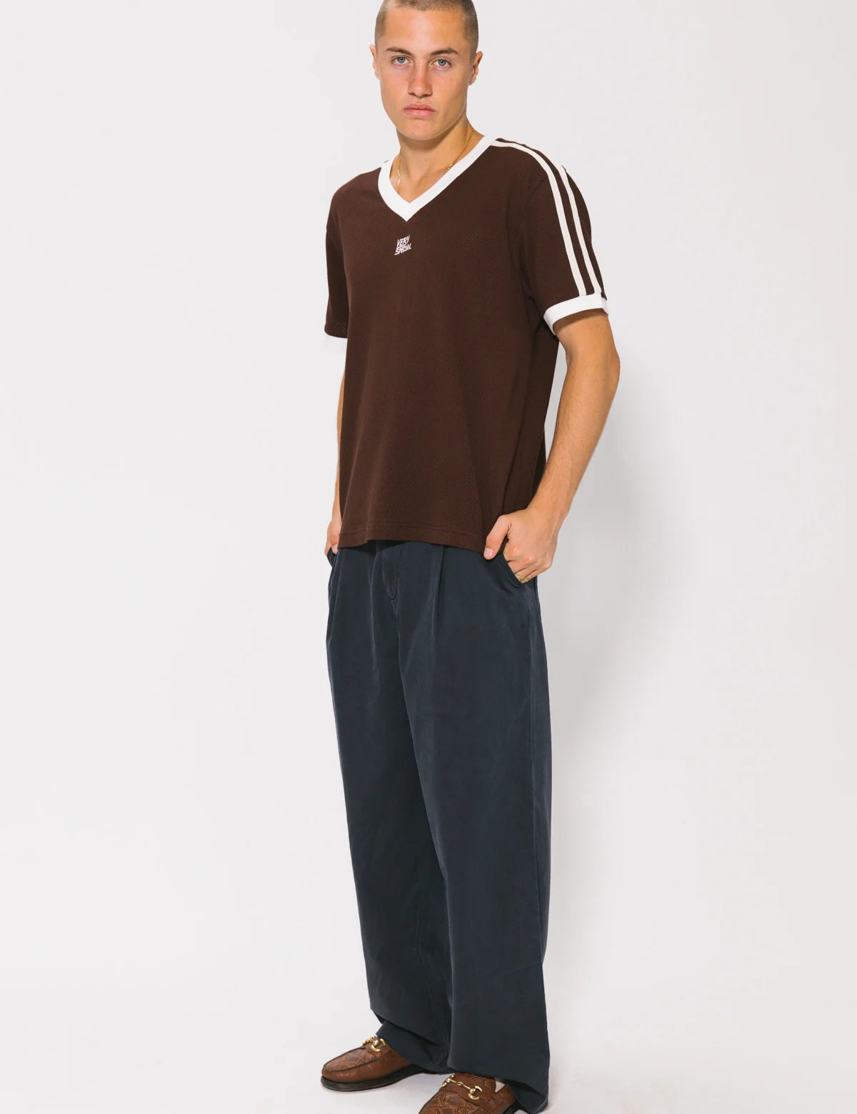 Man wearing a brown t-shirt with white stripes and dark pants on a white background