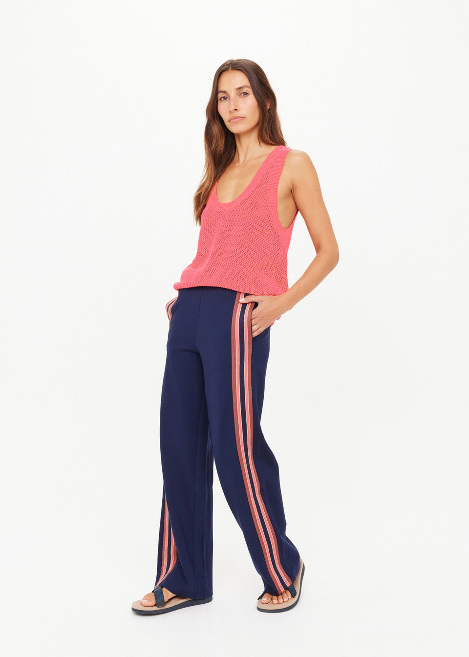 Woman wearing a pink sleeveless top and navy pants with pink stripes on a white background