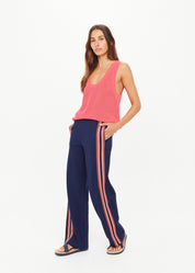 Woman wearing a pink sleeveless top and navy pants with pink stripes on a white background