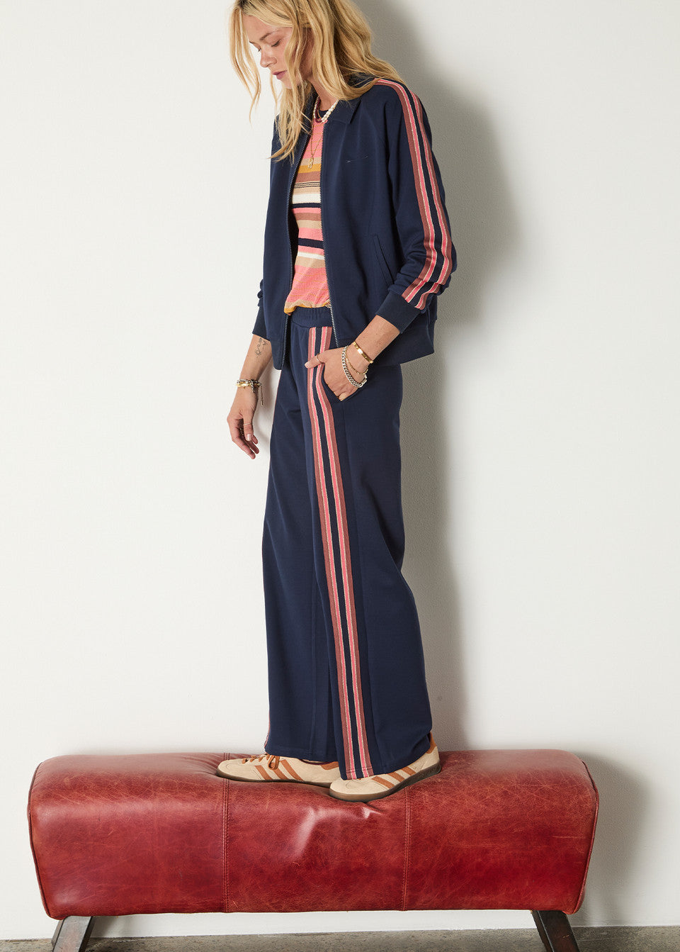 Woman wearing a navy tracksuit with pink stripes on a white background