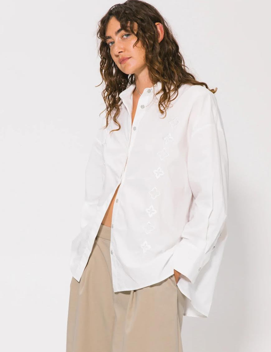 Woman wearing a white shirt and beige pants against a plain background