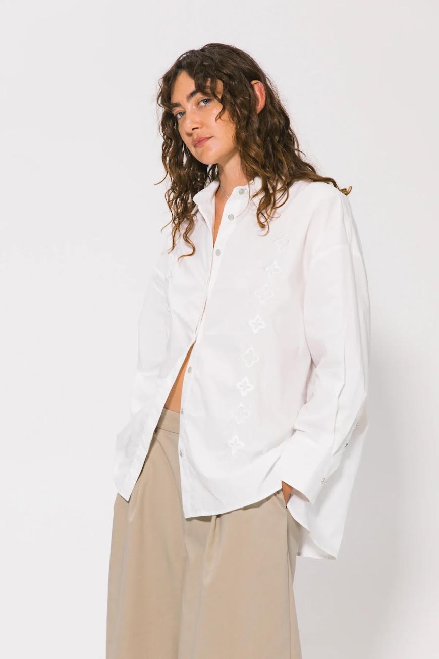 Woman wearing a white shirt and beige pants against a plain background