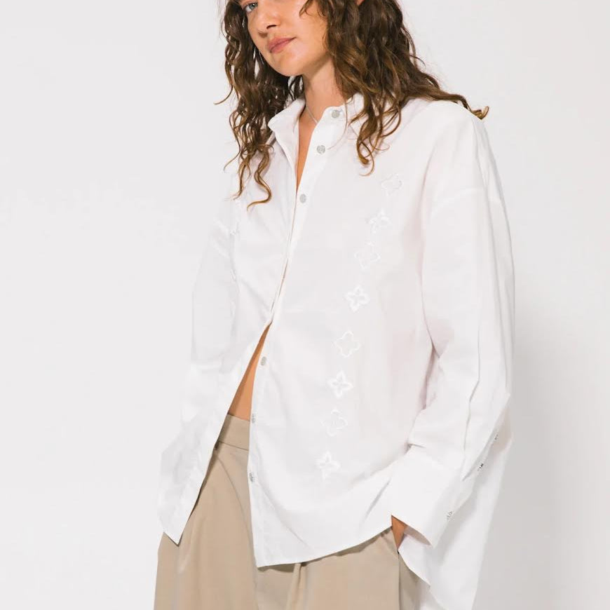 Woman wearing a white shirt and beige pants against a plain background