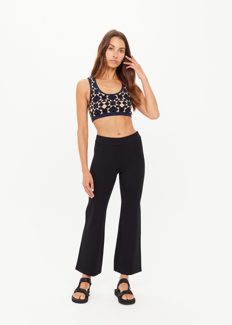 Woman wearing a patterned crop top and black flared pants on a white background