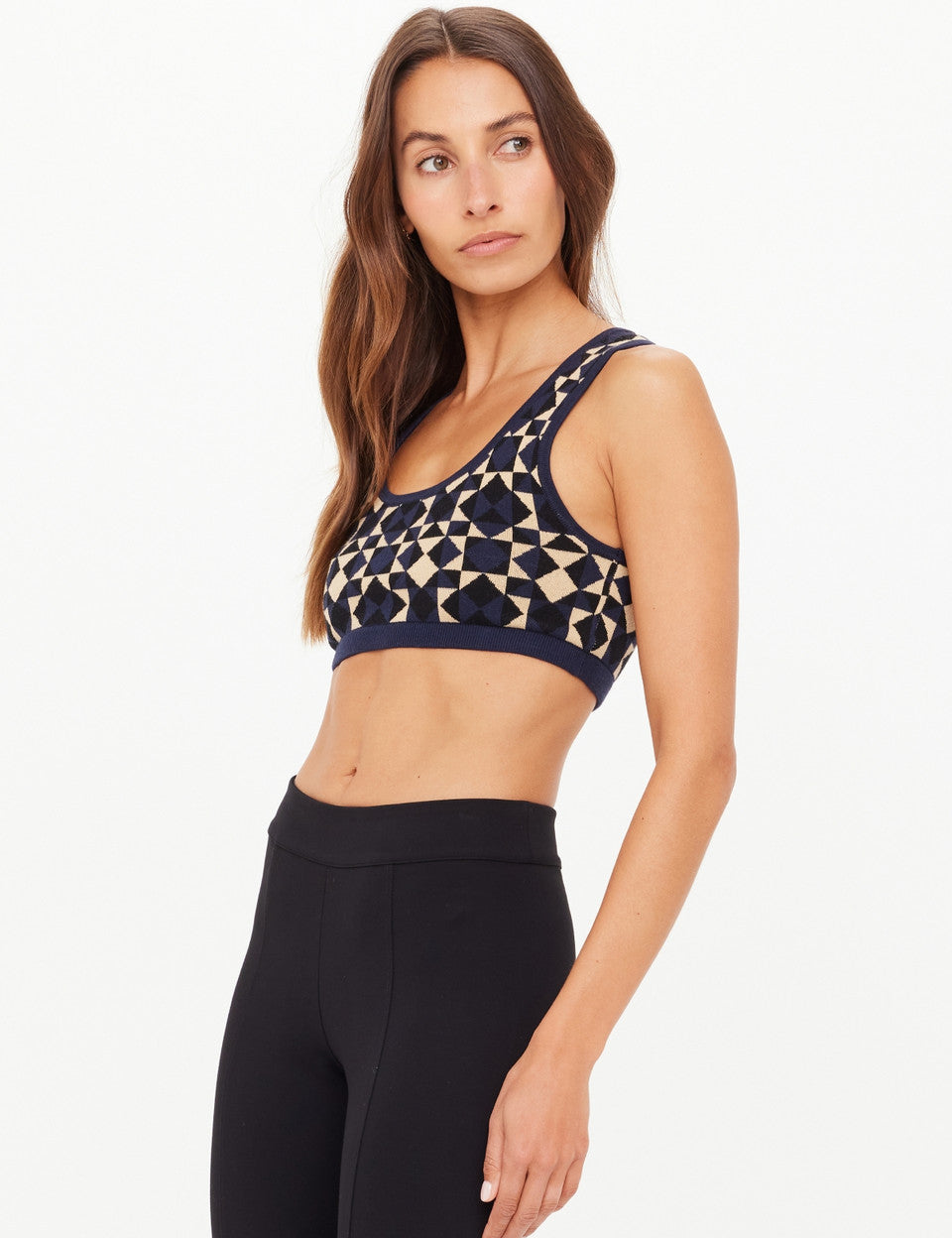 Woman wearing a patterned sports bra and black leggings on a white background