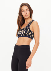 Woman wearing a patterned sports bra and black leggings on a white background