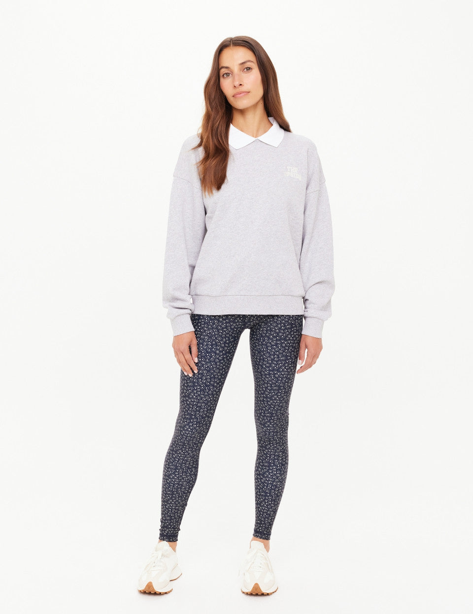 Woman wearing a light gray sweatshirt and patterned leggings on a white background