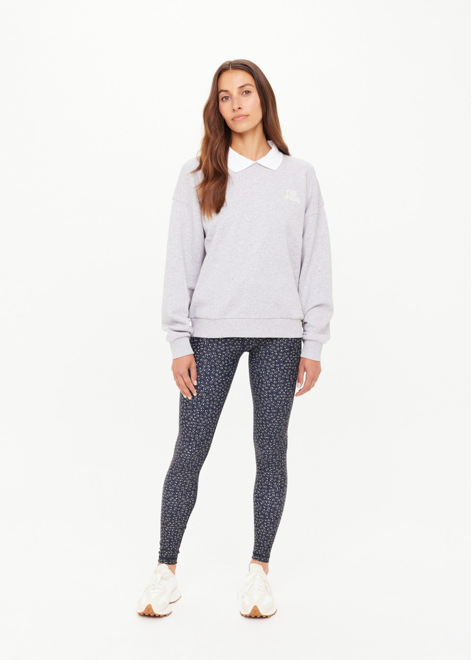 Woman wearing a light gray sweatshirt and patterned leggings on a white background