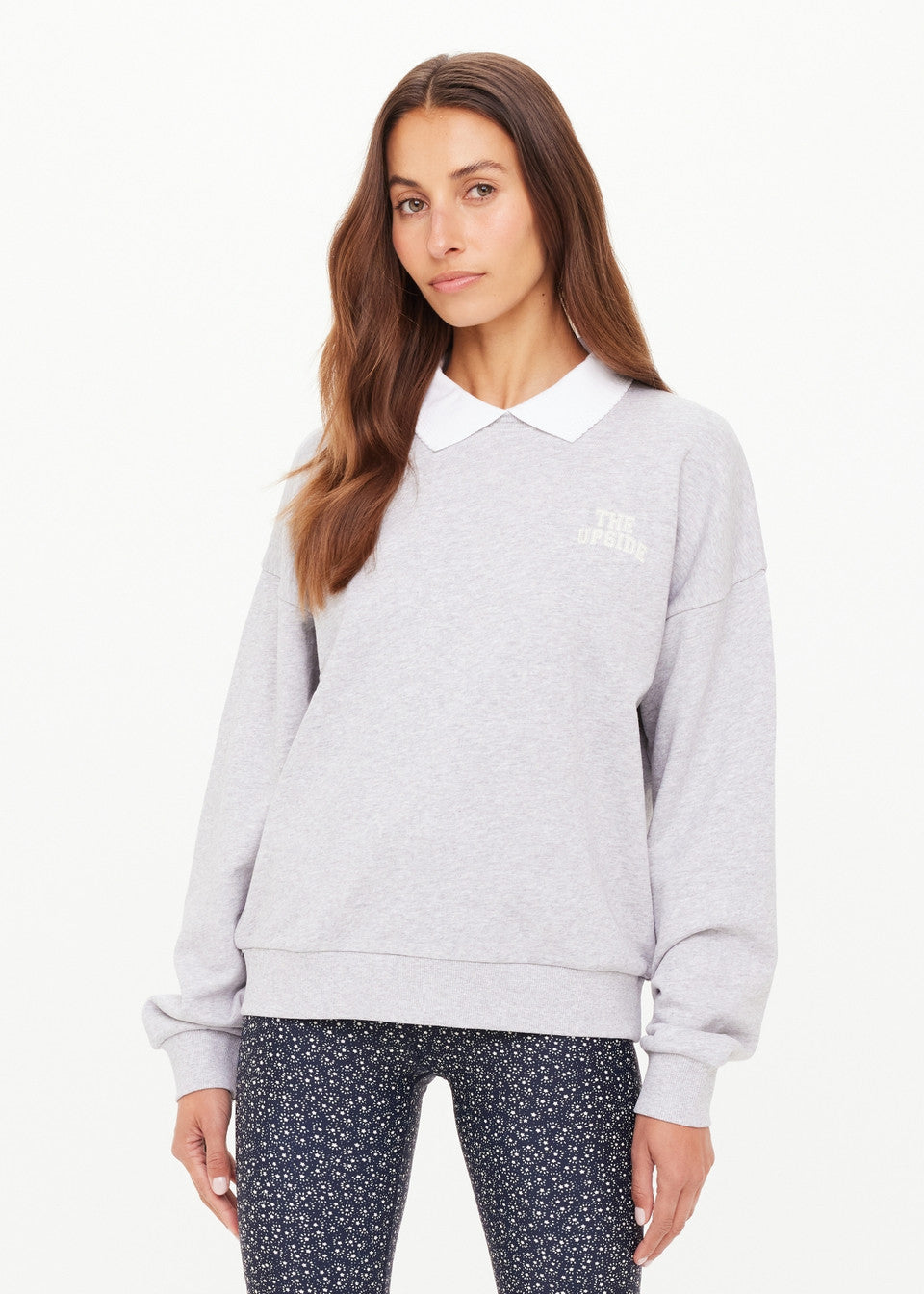 Woman wearing a light gray sweatshirt with a collar and navy patterned pants on a white background