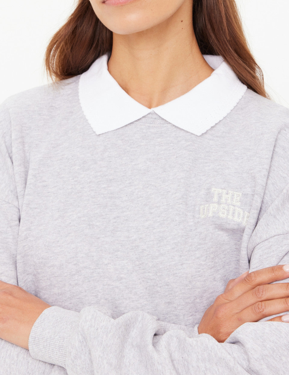 Person wearing a gray sweater with a white collar and embroidered logo.