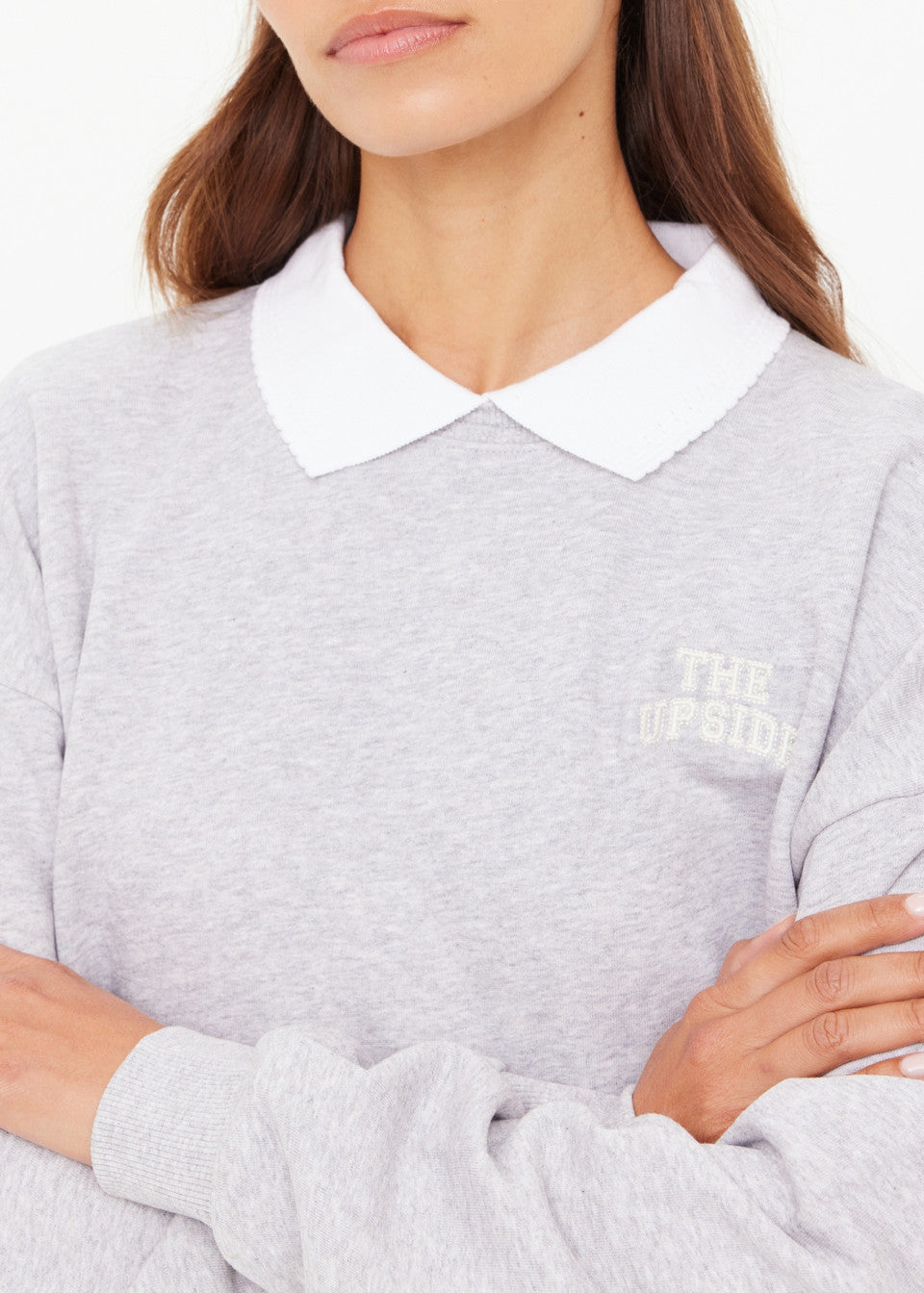 Person wearing a gray sweater with a white collar and embroidered logo.