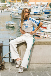 Woman in a tracksuit sitting by a waterfront with boats in the background